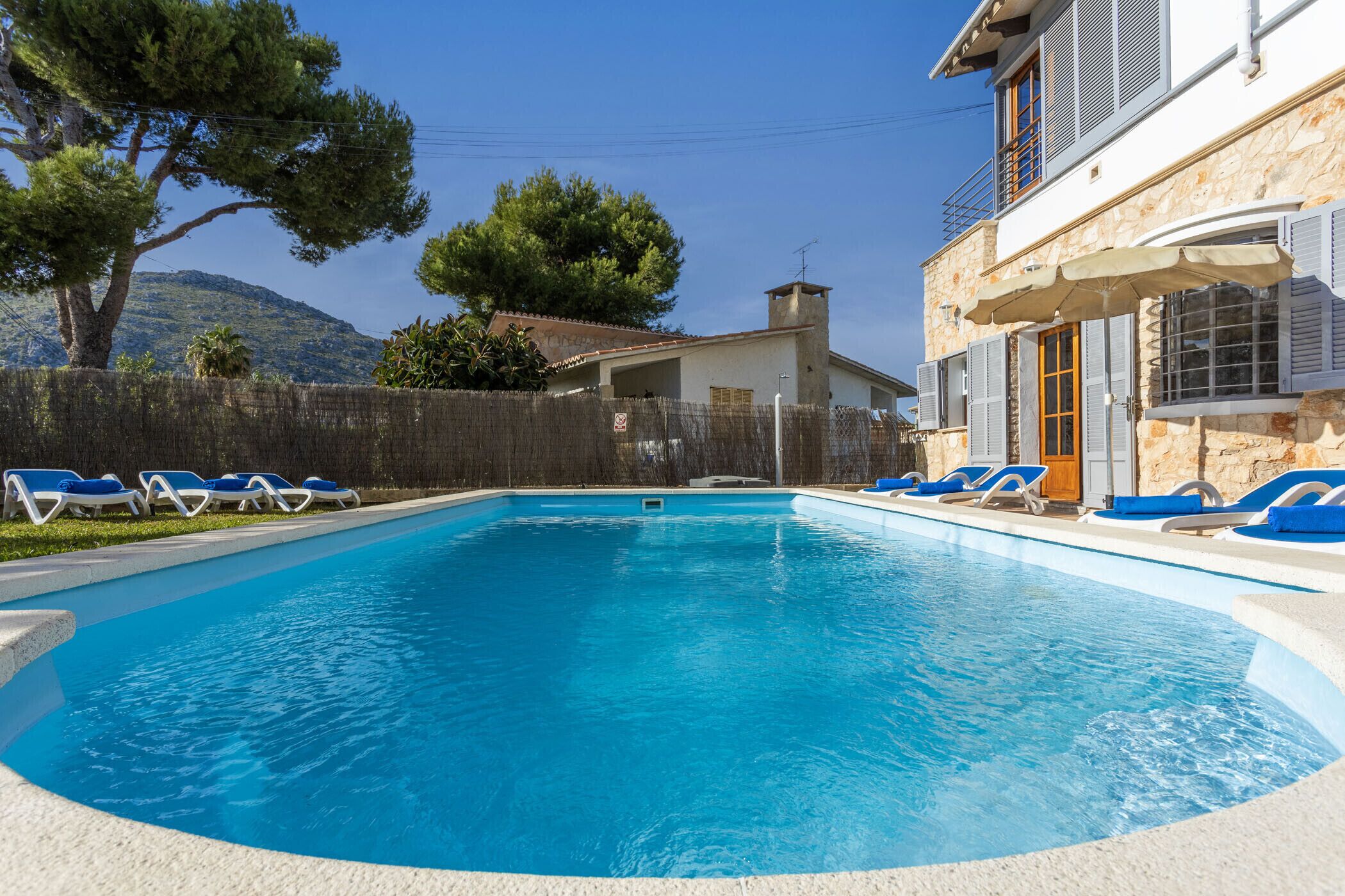 A swimming pool with blue water, surrounded by lounge chairs and a stone building with a balcony.
