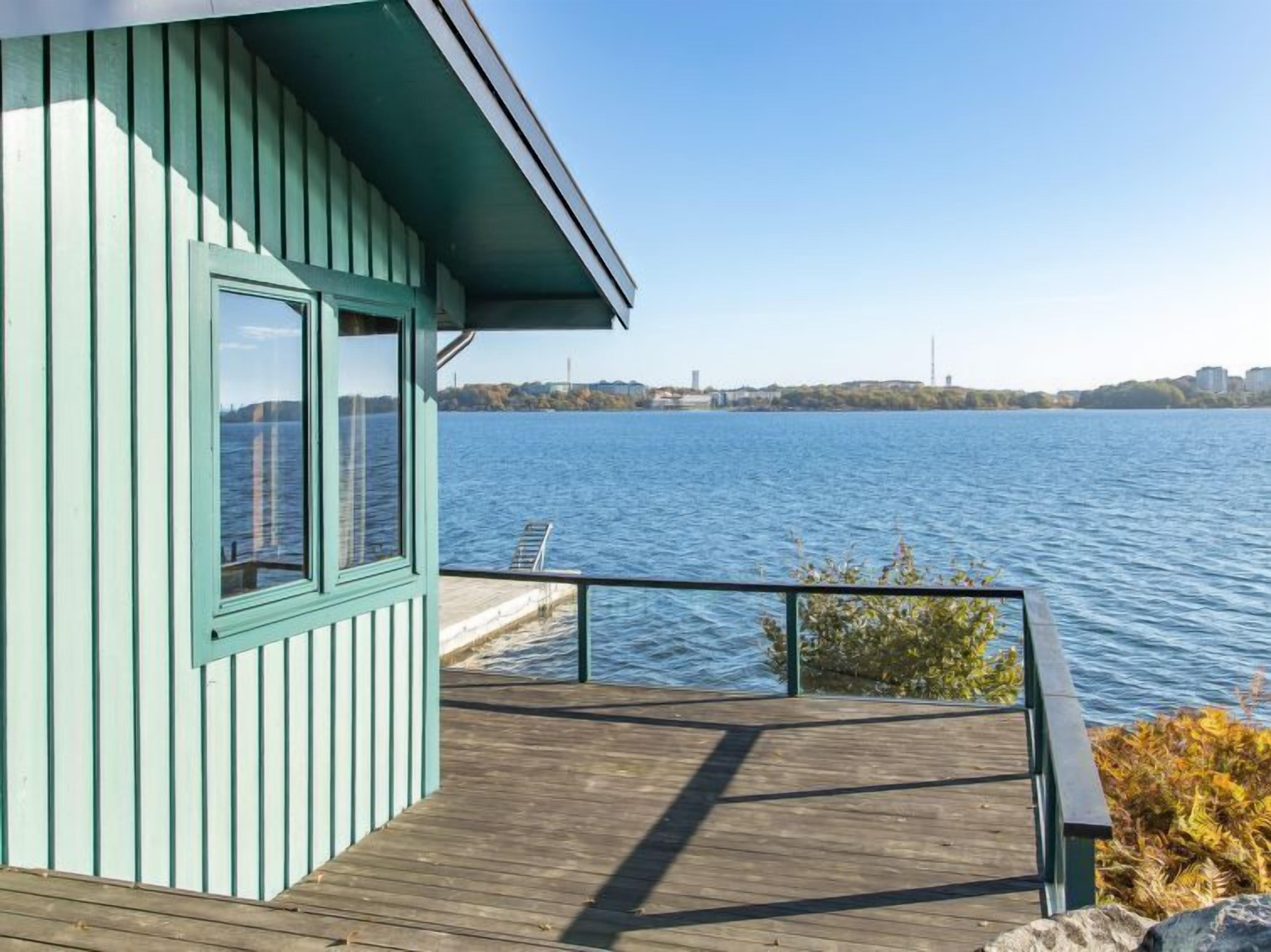 Una terraza de madera con vista a un lago tranquilo y un horizonte lejano de la ciudad.