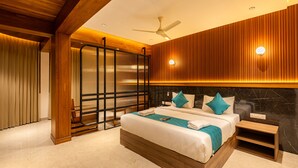 Una habitación de hotel moderna con una cama grande, detalles de madera, un ventilador de techo y un aplique de pared.