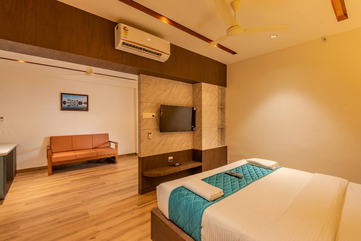 A hotel room with a bed, a TV mounted on the wall, a wooden bench, and a ceiling fan.