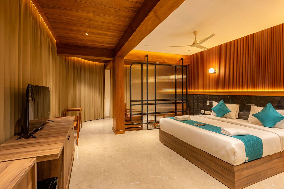 A modern hotel room with a wooden ceiling, a bed with teal bedding, a desk with a computer, and a sliding door.