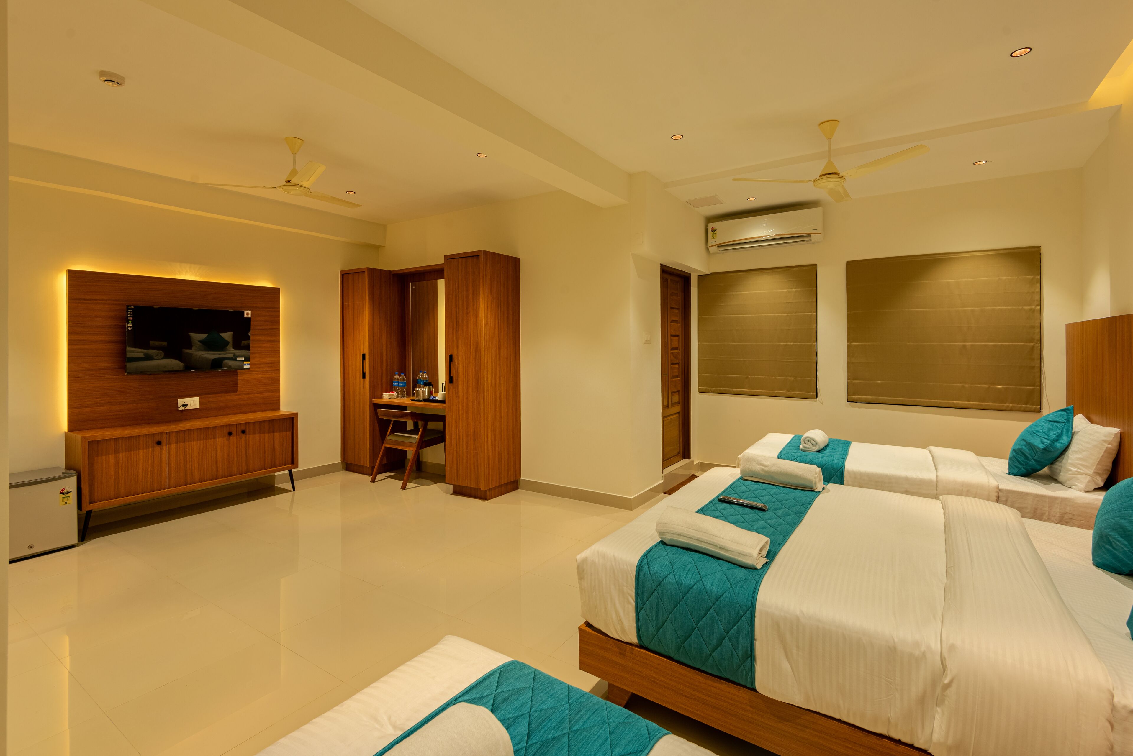 A hotel room with two beds, a desk, a TV, and a ceiling fan.