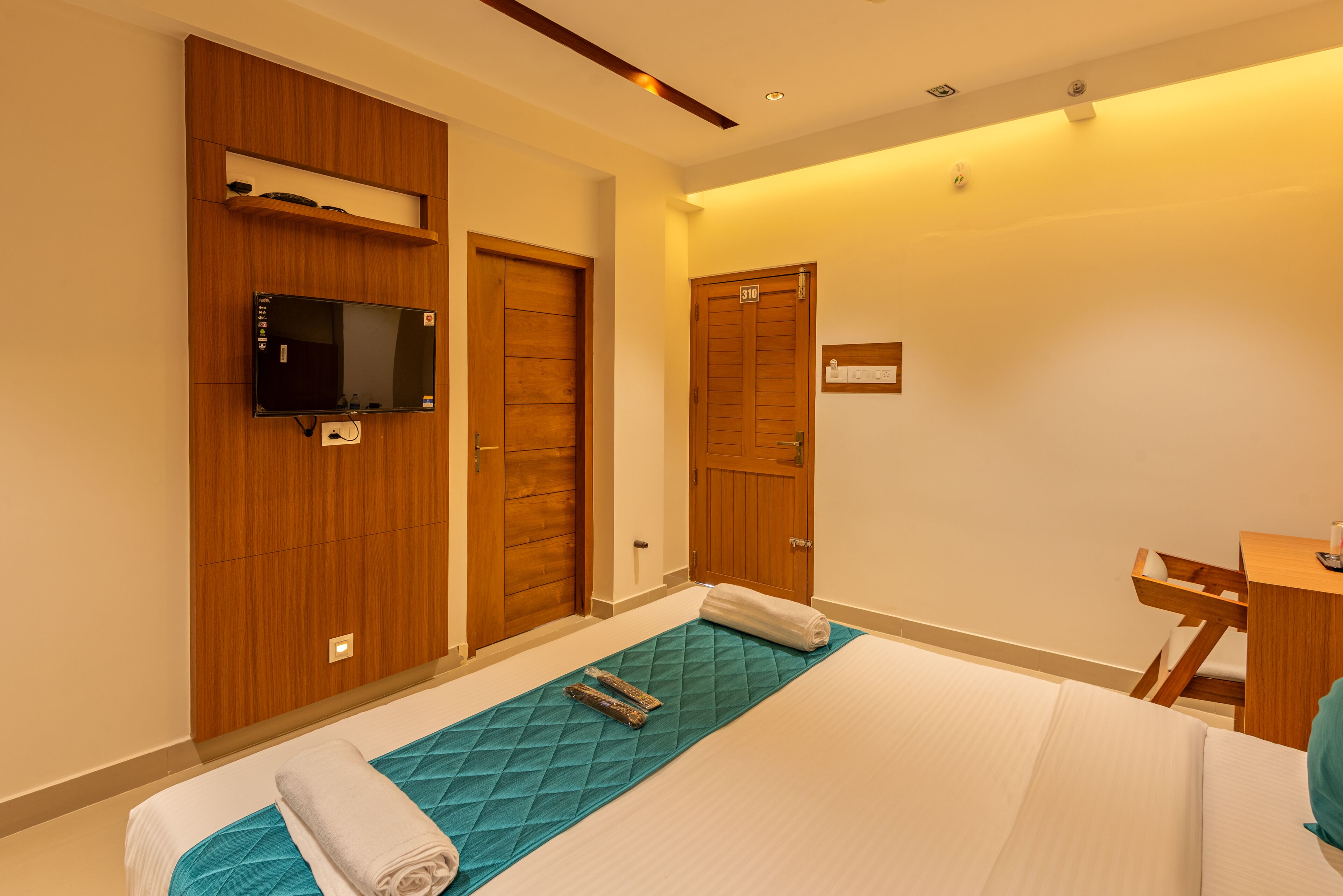 Una habitación de hotel con cama, televisor montado en la pared, puertas de madera y un escritorio con silla.