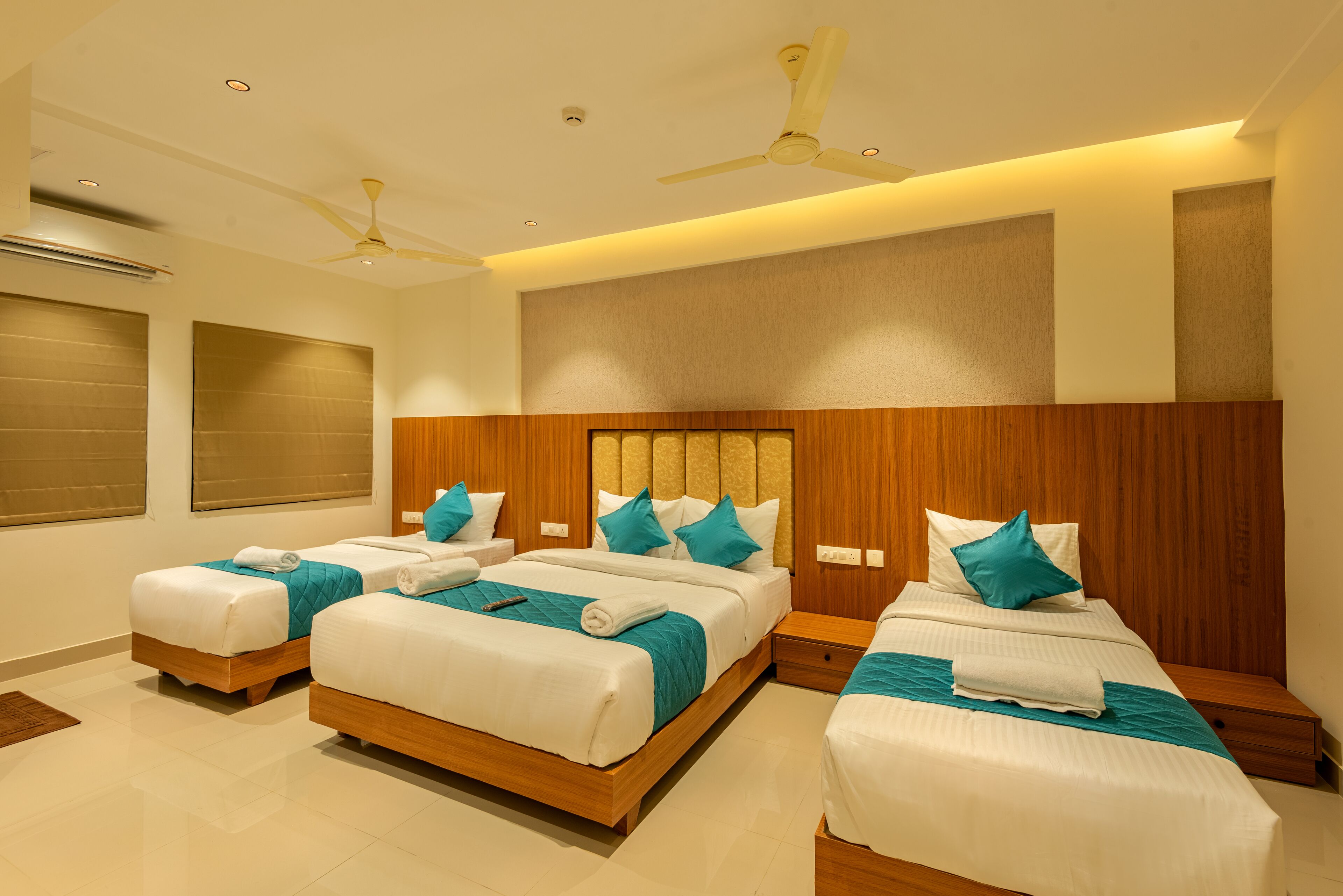 A hotel room with three beds, wooden headboards, and ceiling fans.