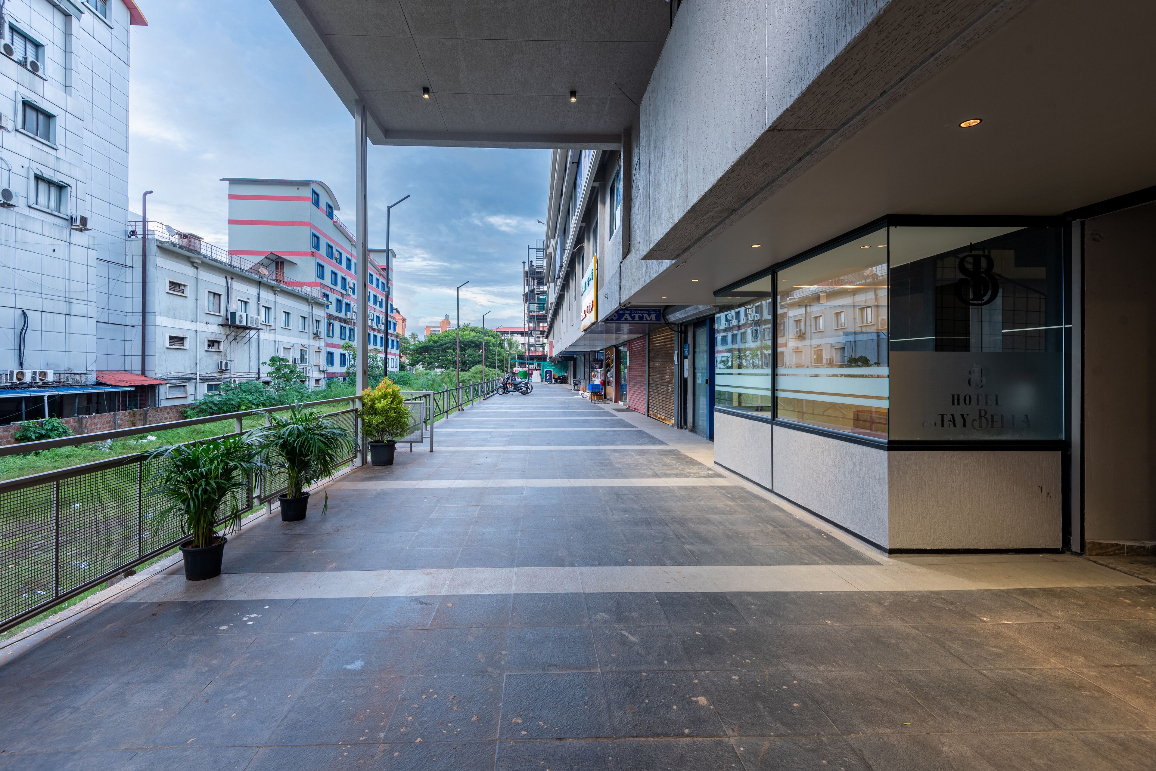 A modern hotel corridor with a glass facade, potted plants, and a view of the cityscape.