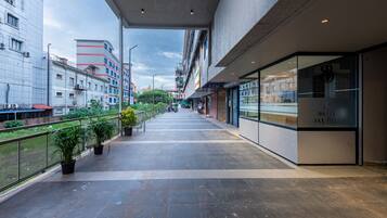 A modern hotel corridor with a glass facade, potted plants, and a view of the cityscape.