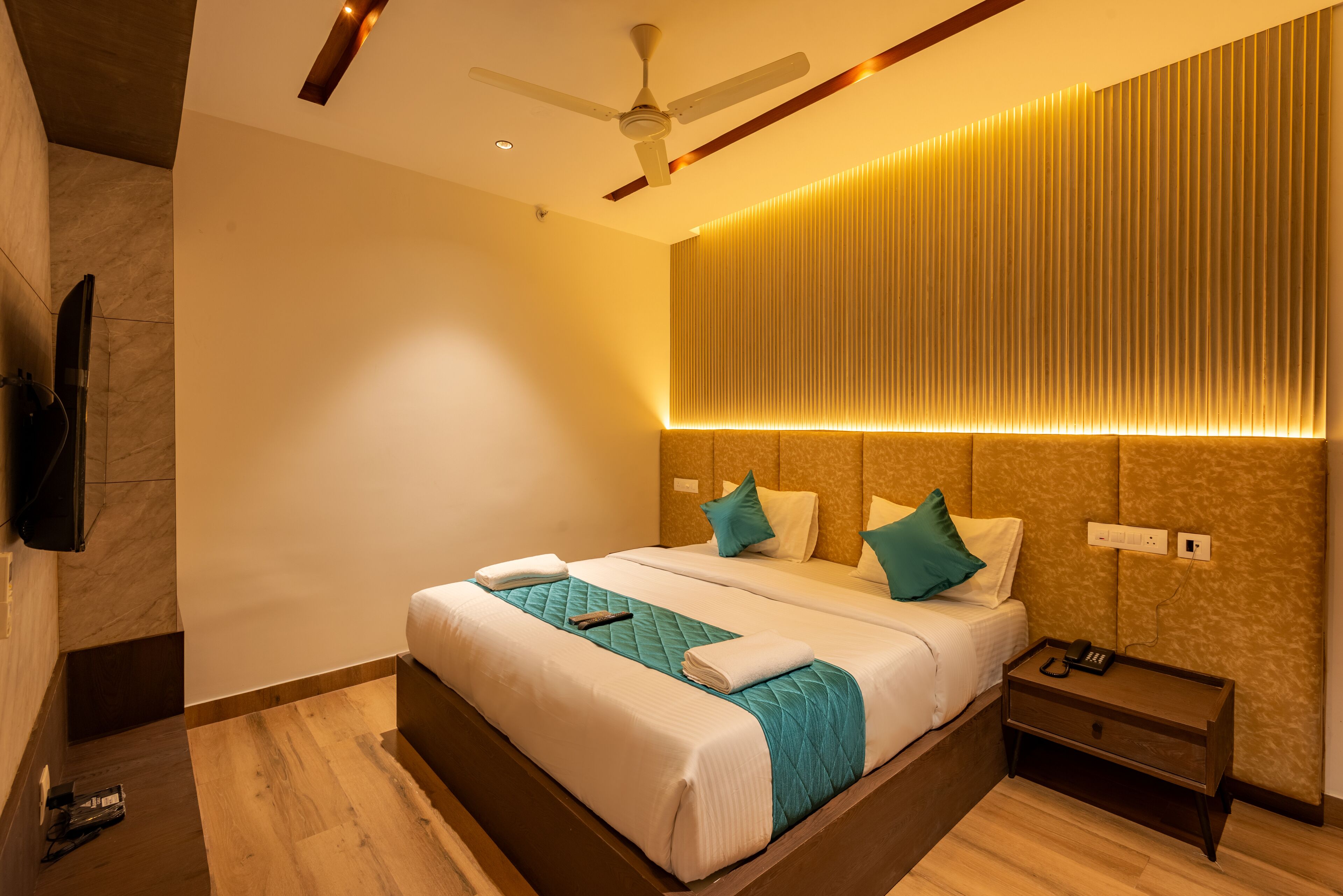 Une chambre d’hôtel moderne avec un grand lit, une table de chevet, un ventilateur de plafond et un téléviseur fixé au mur.
