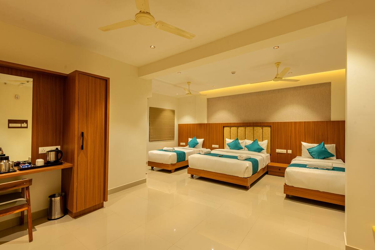 A hotel room with three beds, a wooden desk, a mirror, and ceiling fans.