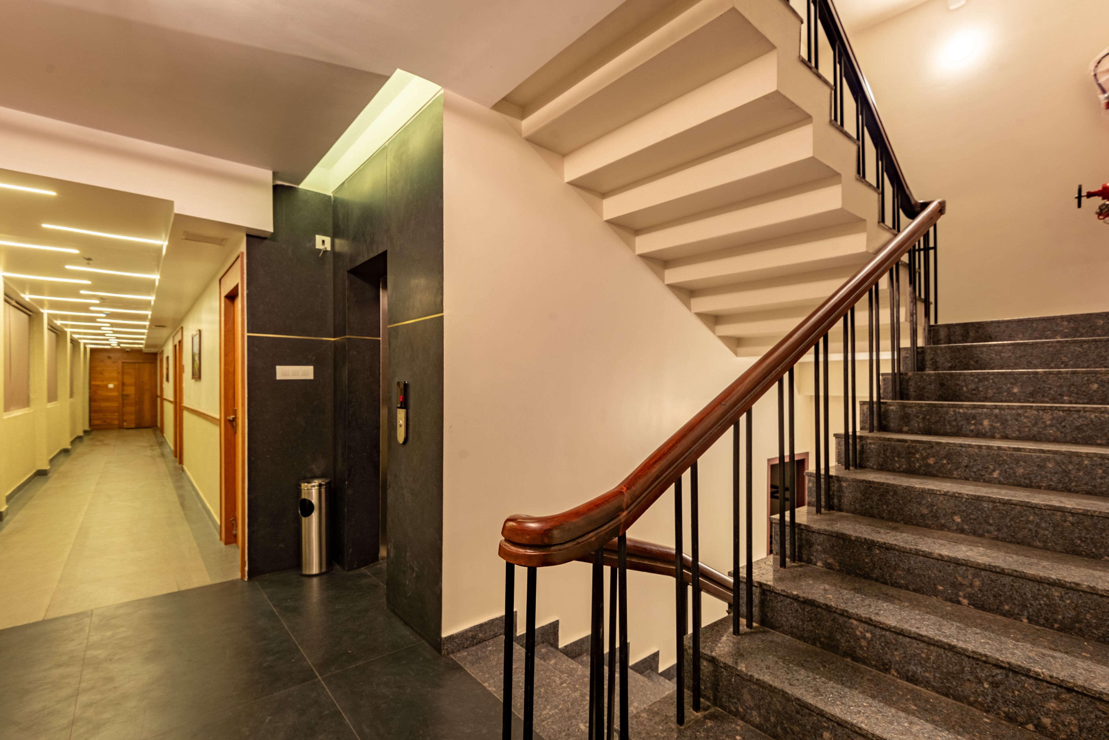 A modern hotel lobby with a staircase, a trash bin, and a wooden door.