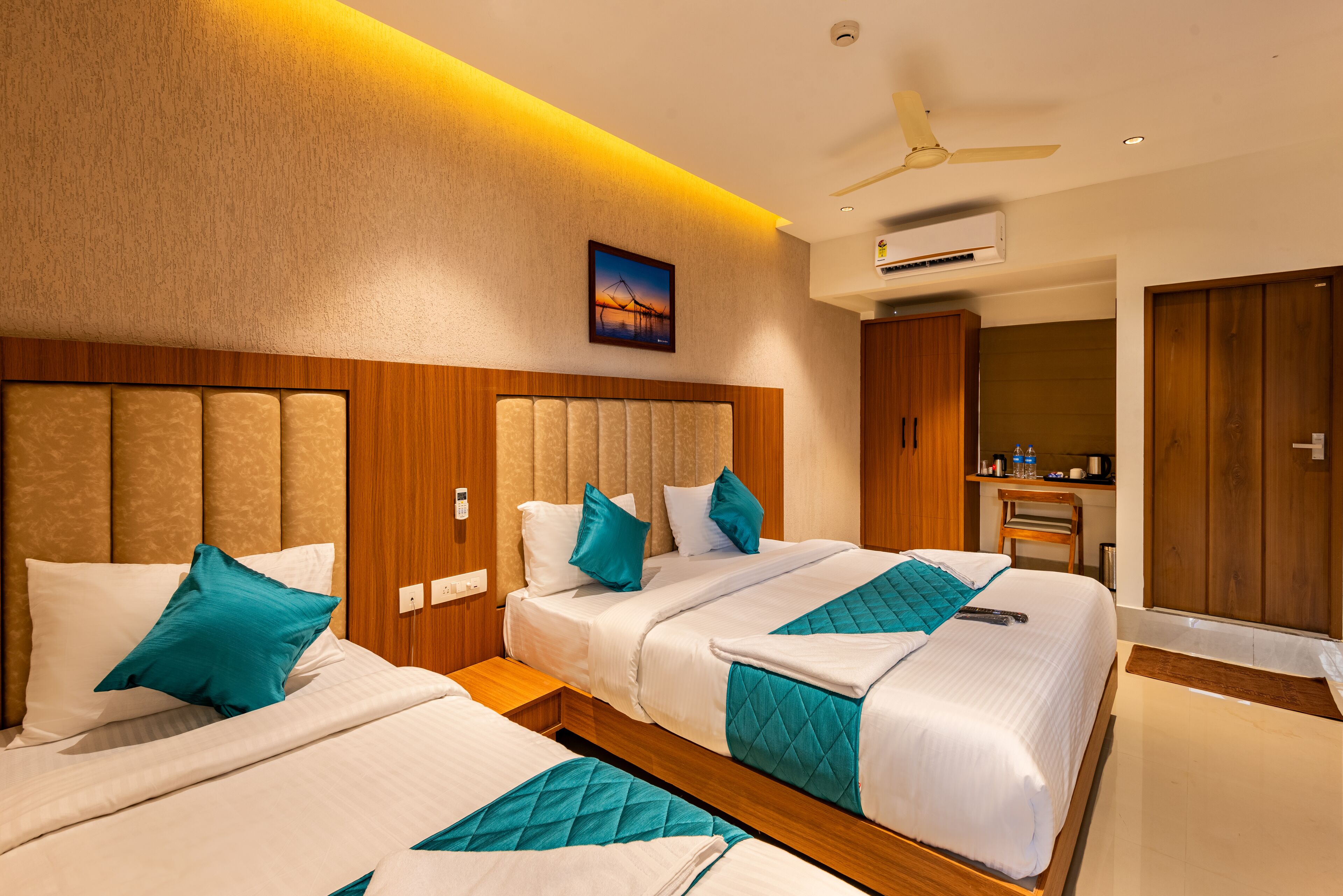 A hotel room with two beds, a ceiling fan, an air conditioning unit, and a painting on the wall.