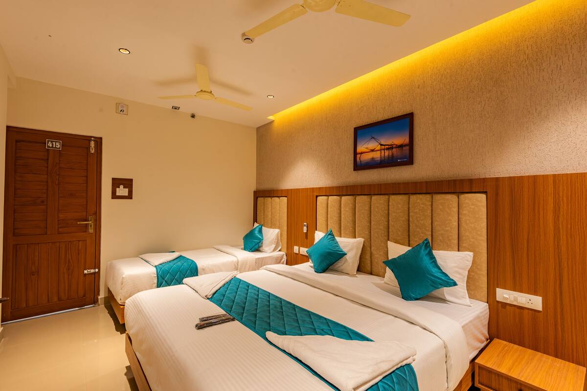 A hotel room with two beds, a ceiling fan, a painting, and a wooden door.