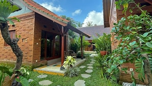 A traditional brick house with a tiled patio, a covered porch, and a small garden area with stepping stones and potted plants.