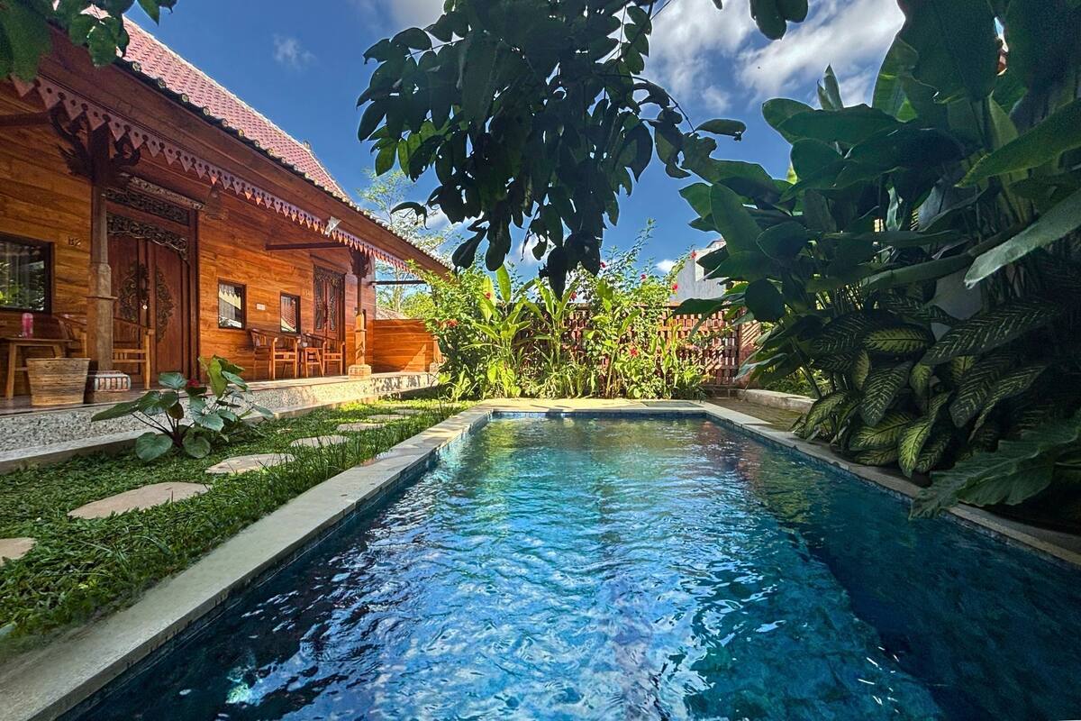 A wooden house with a swimming pool surrounded by lush greenery.