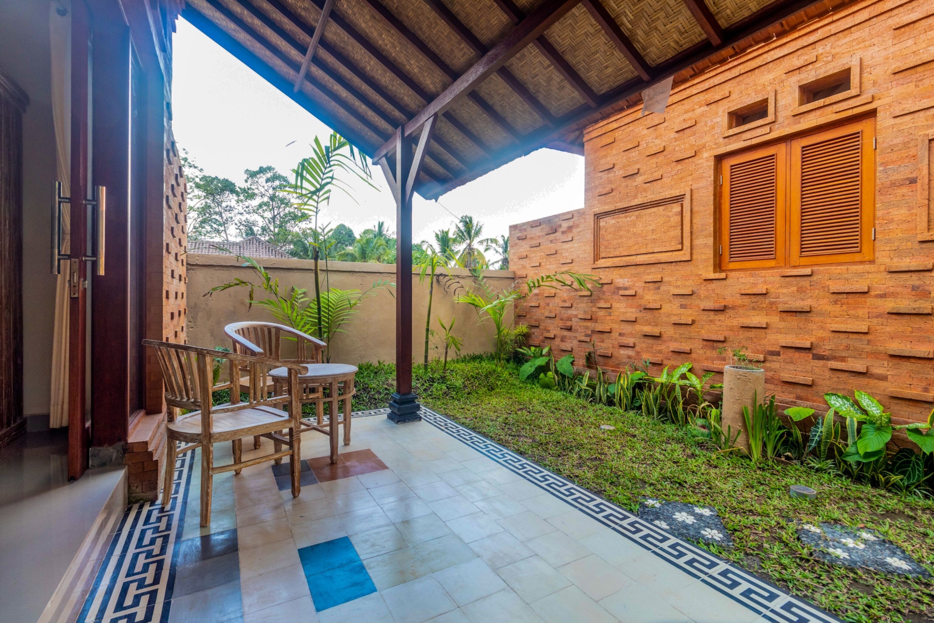 Un patio techado con pared de ladrillo, una mesa y sillas de madera, y piso de baldosas con diseño geométrico.