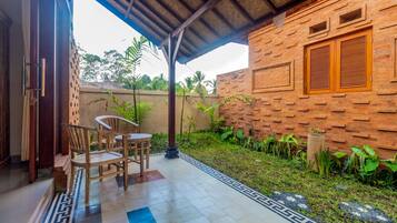 Un patio techado con pared de ladrillo, una mesa y sillas de madera, y piso de baldosas con diseño geométrico.
