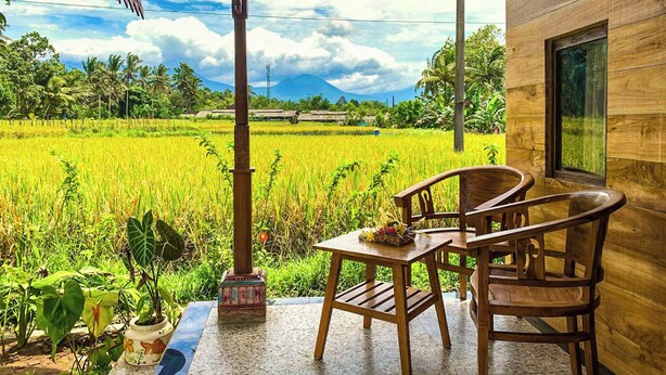 A wooden room with a table and chairs, a window, and a view of a rice field and mountains.
