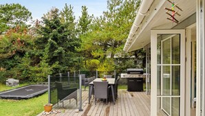 Une terrasse en bois avec des meubles d’extérieur, un barbecue et une porte vitrée donnant sur un espace abrité.