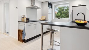 Une cuisine moderne dotée d’un plan de travail noir, d’appareils électroménagers en acier inoxydable et d’une fenêtre offrant une vue sur la verdure environnante.