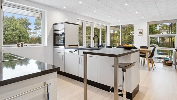 Une cuisine moderne dotée d’un îlot central, de grandes fenêtres et offrant une vue sur les arbres.