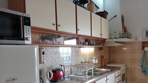 A kitchen with a microwave, coffee maker, and dishwasher. There is a sink with a faucet and a dish rack. The kitchen has white cabinets and a tiled backsplash.