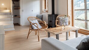 Ein gemütliches Zimmer mit Holzbalkendecke, einer Couch, einem Tisch mit einer Vase und Blick ins Freie.