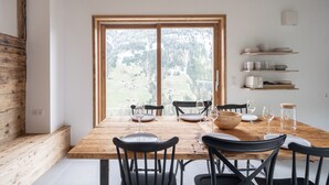 Ein Essbereich mit einem Holztisch, gedeckt für sechs Personen, schwarzen Stühlen und einem großen Fenster mit Blick auf eine bewaldete Landschaft.
