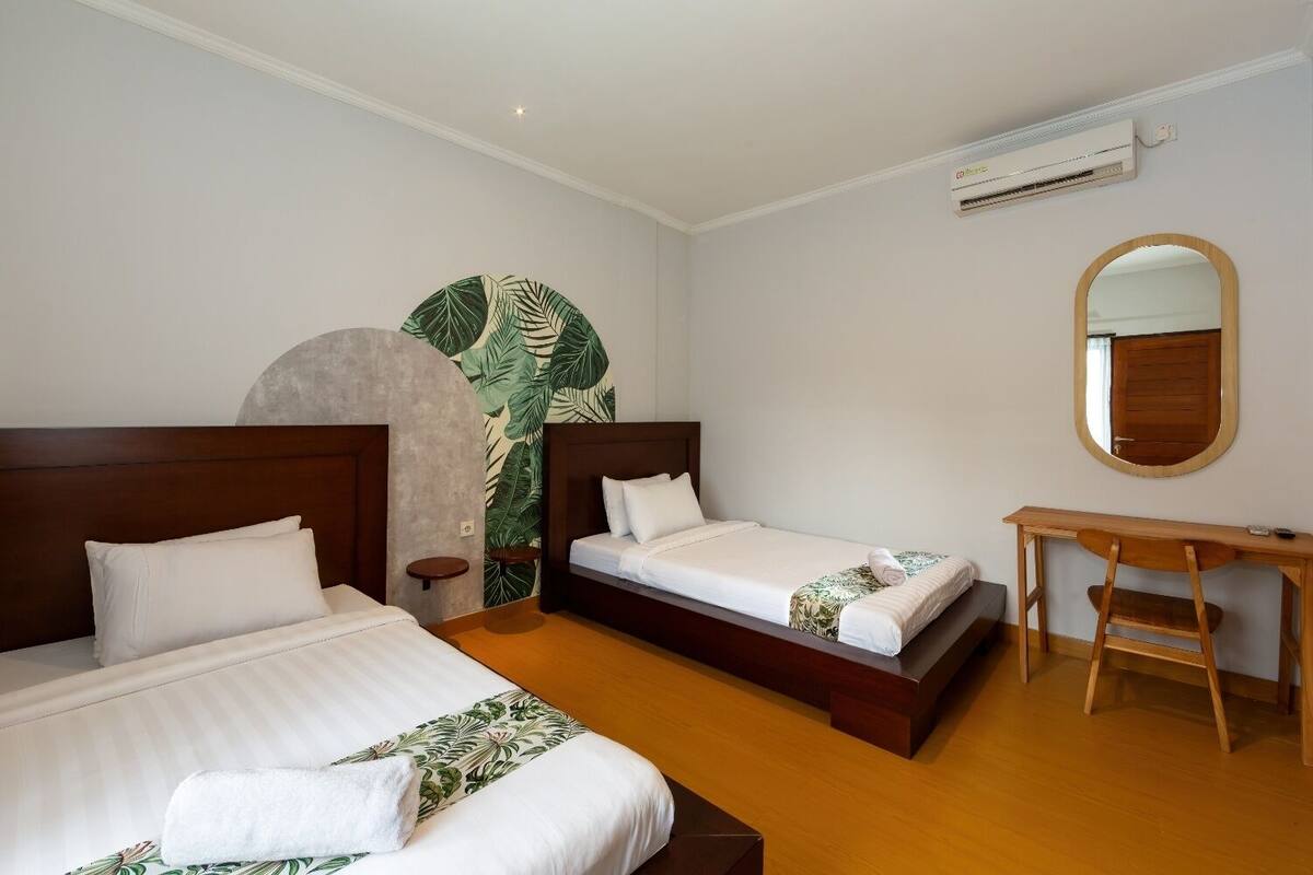 Habitación de hotel con dos camas, un escritorio, un espejo y un aire acondicionado.