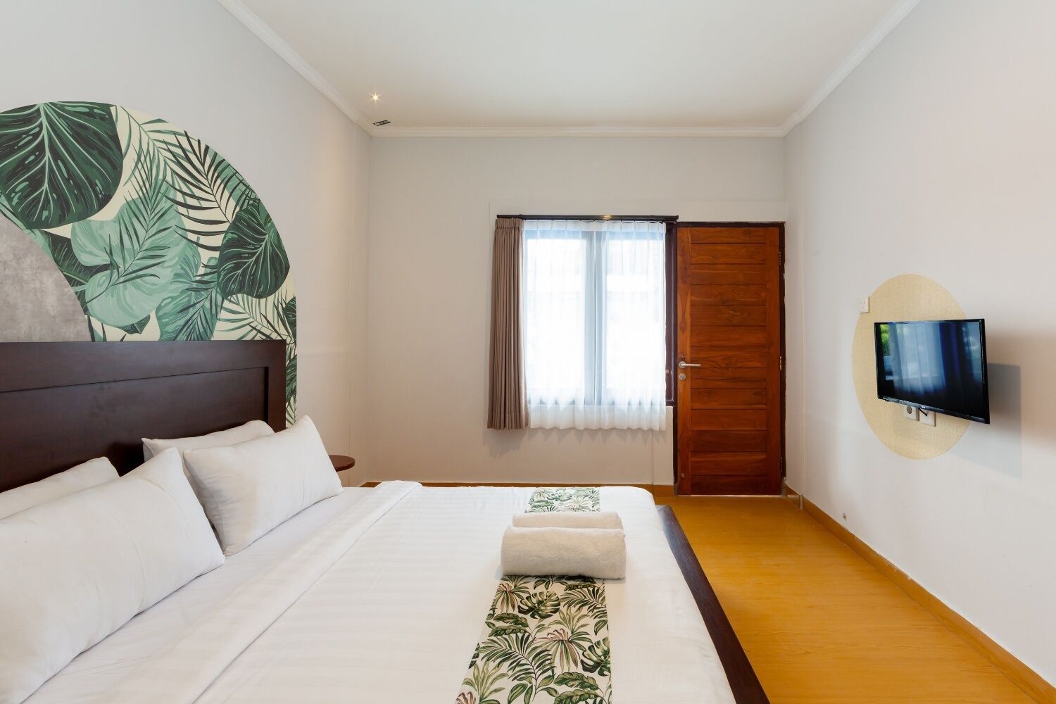 Una habitación de hotel con una cama grande, un televisor montado en la pared y una ventana con cortinas.
