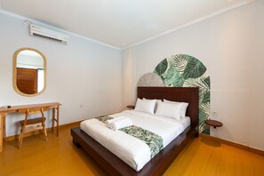 Une chambre à coucher comprenant un lit, un bureau en bois, une chaise, un appareil de climatisation et un mur orné d’un motif de feuilles.