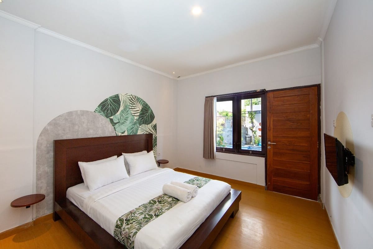 Un dormitorio con cama de madera, un ventanal con cortinas y un televisor montado en la pared.
