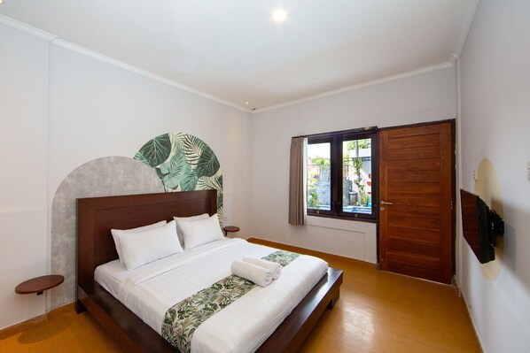 Une chambre avec un lit en bois, une grande fenêtre avec des rideaux et un téléviseur fixé au mur.