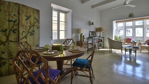 A spacious dining area with a round table, wicker chairs, and a view of the outdoors through large windows. - Sea Breeze Apartment (Floriana)