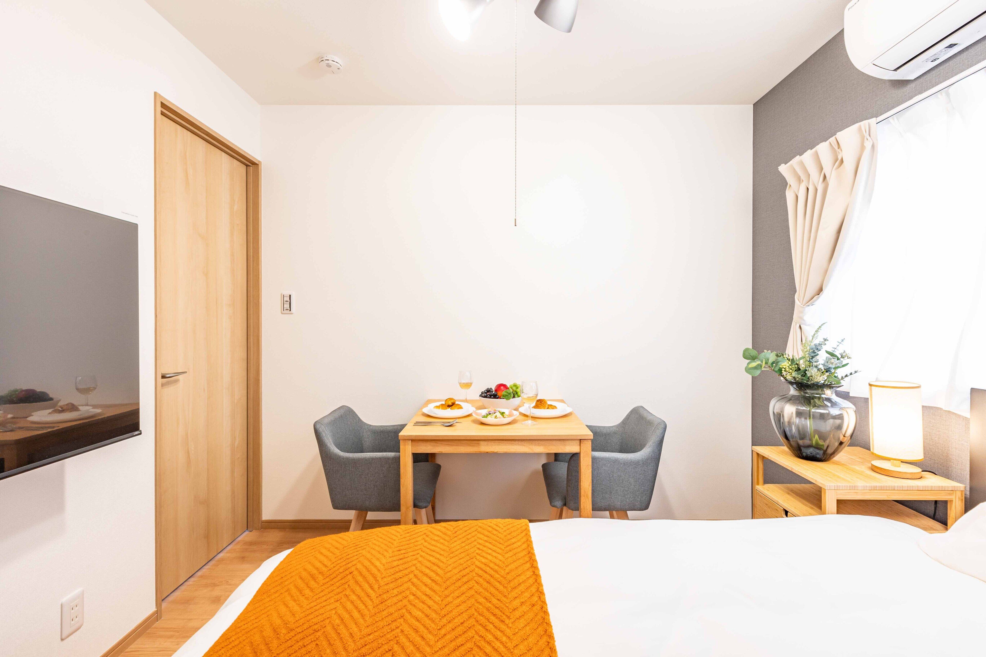 Een hotelkamer met een bed, een eettafel met stoelen, een aan de muur bevestigde televisie en een bijzettafeltje met een lamp en vaas.