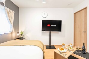 A modern hotel room with a bed, a flat-screen TV mounted on the wall, a small table with breakfast items, and a wooden door. - Precious Terrace (Osaka)