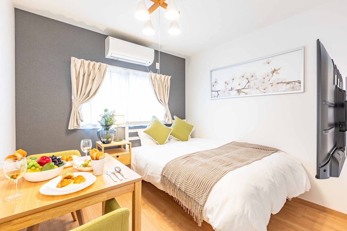 Quarto de hotel moderno com cama, mesa de refeições com café da manhã, televisão e janela com cortinas.