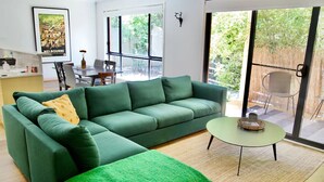 Una sala de estar moderna con un sofá verde, una mesita redonda y un ventanal con vistas al exterior.