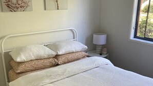 Una cama bien hecha con ropa de cama blanca y estampada, una lámpara de noche y un cuadro en la pared.
