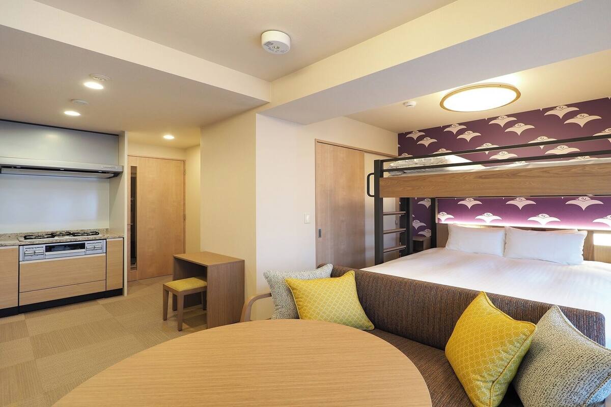 A hotel room with a bunk bed, a kitchenette, a dining table, and a sofa.