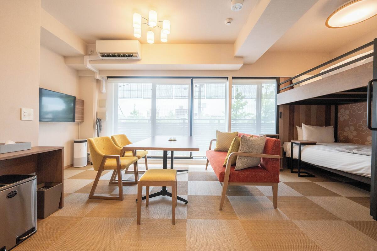 A compact hotel room with a bunk bed, a desk with a chair, a sofa, and a television.