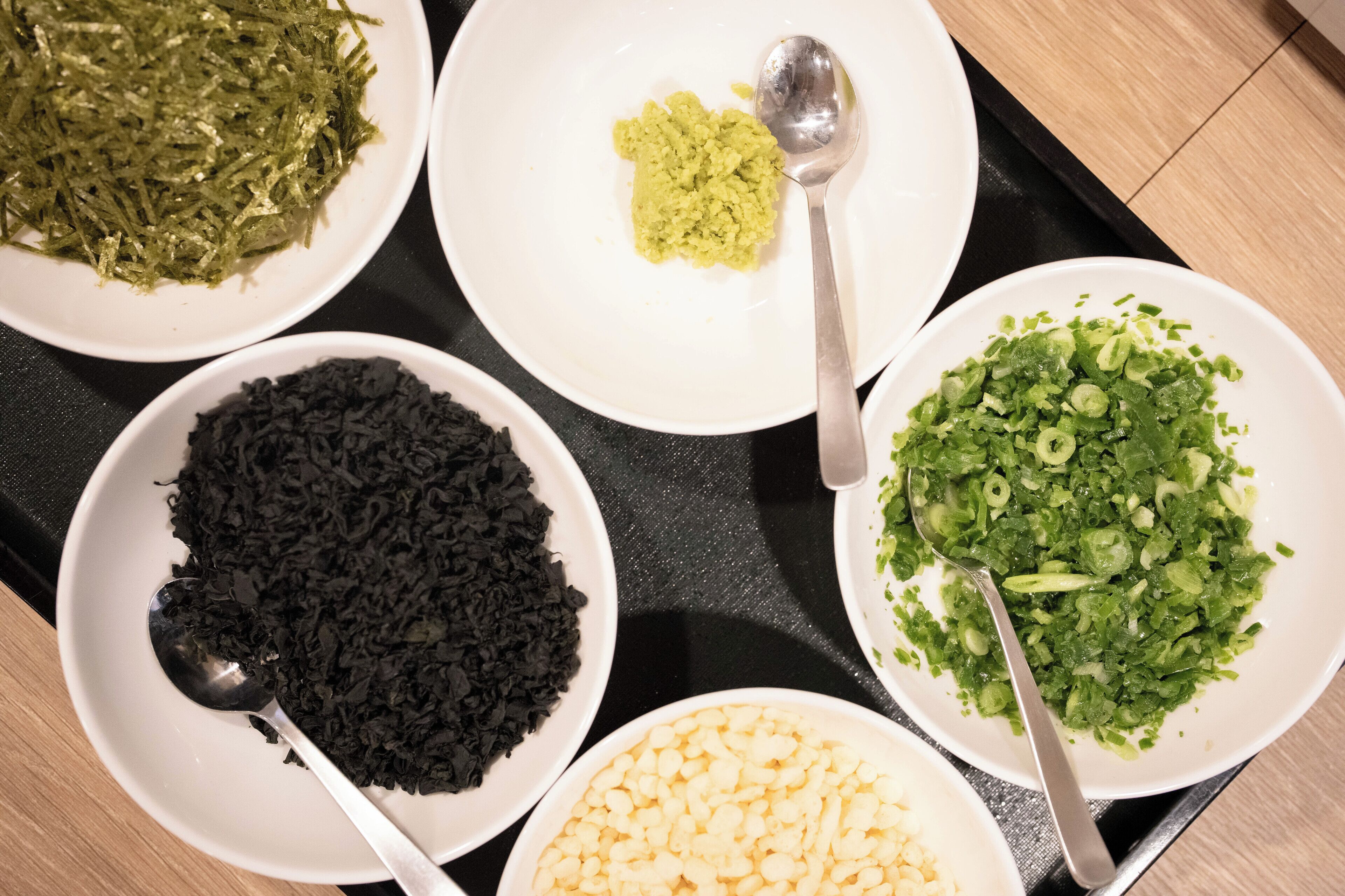 Una bandeja con cuatro cuencos blancos que contienen diferentes alimentos: vegetales verdes picados, puré de vegetales verdes, vegetales verdes en trozos y arroz negro.