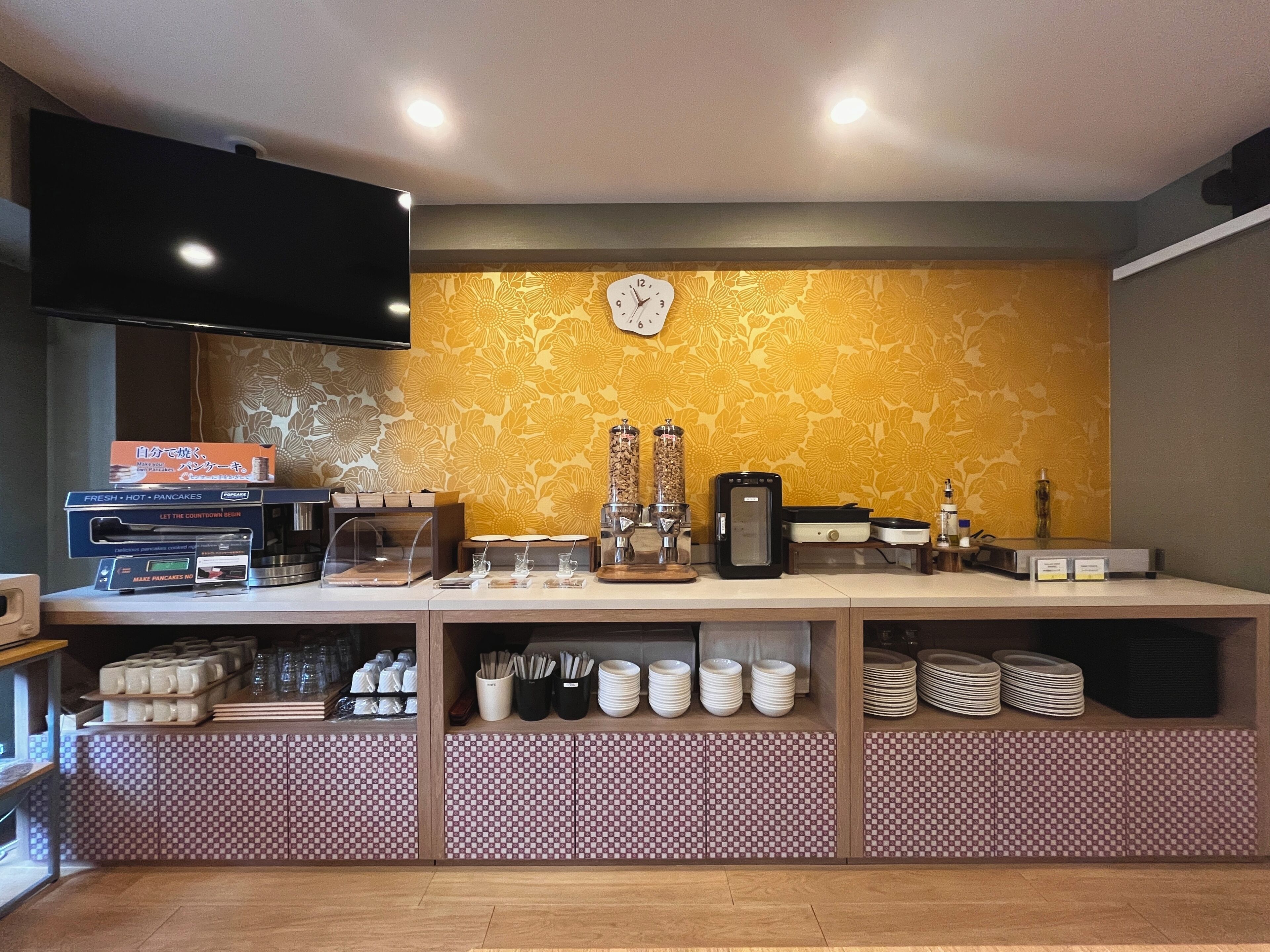 Een ontbijtbalk met een klok, een koffieapparaat en een aan de muur bevestigde televisie.
