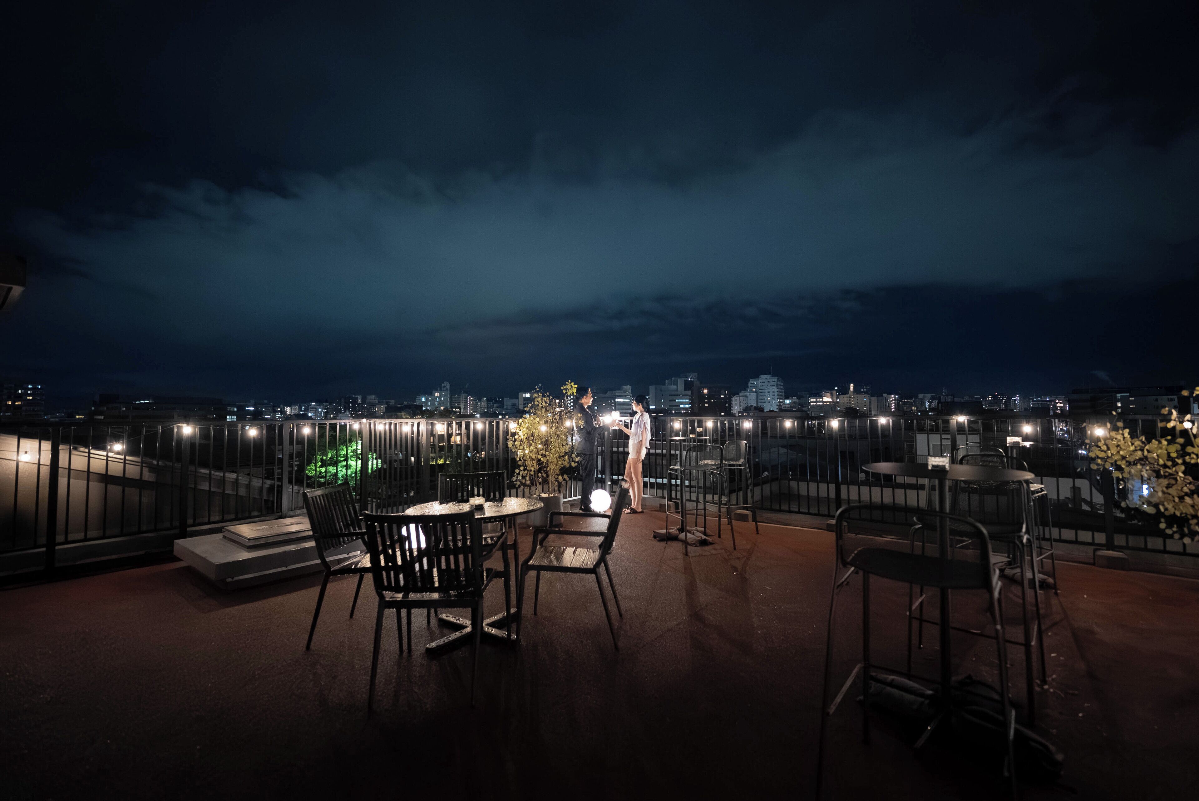 A rooftop terrace with outdoor seating and a view of the city skyline at night.