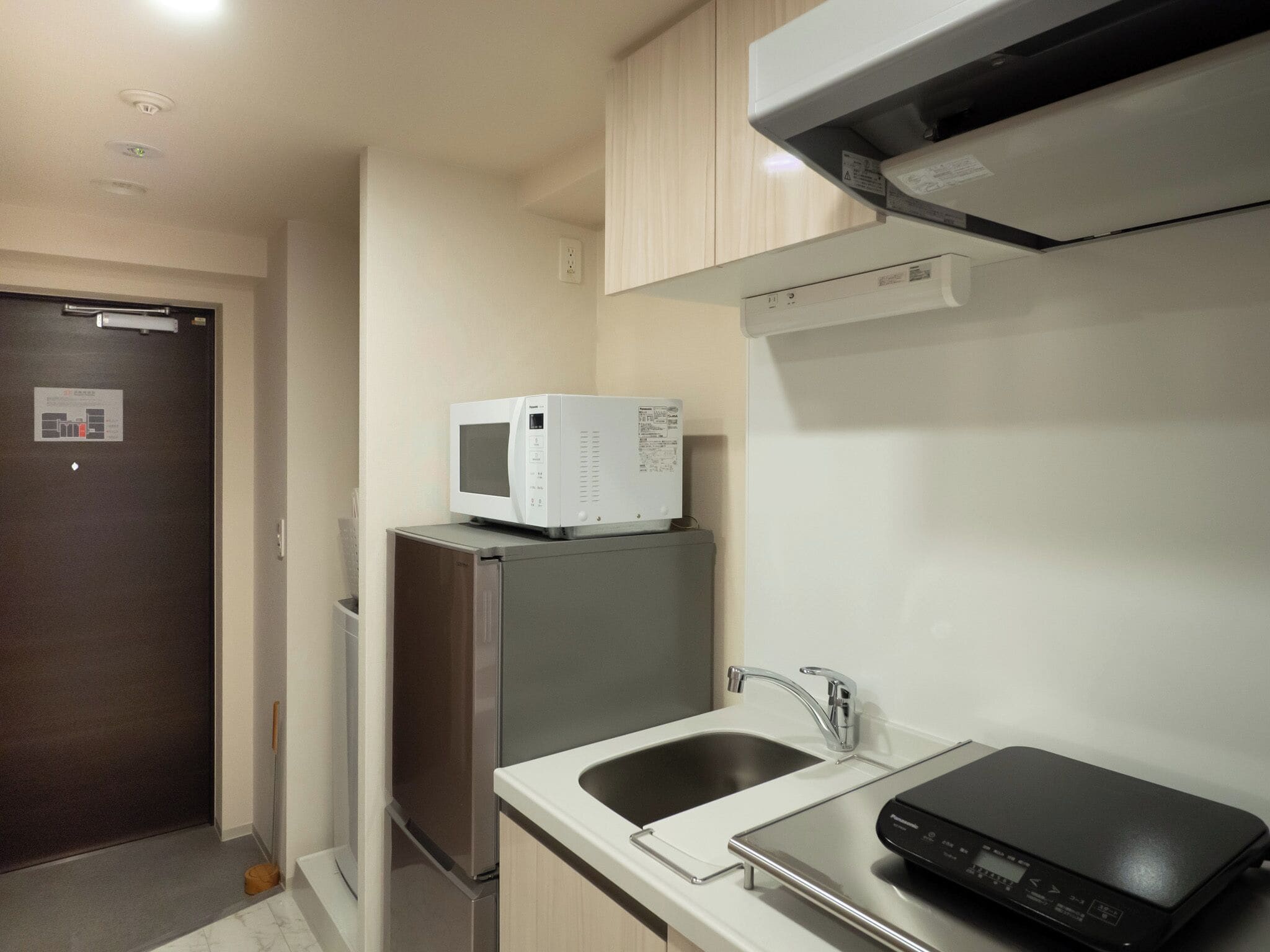 A compact kitchen with a built-in microwave, a stainless steel refrigerator, a sink, and a black portable device on the counter.