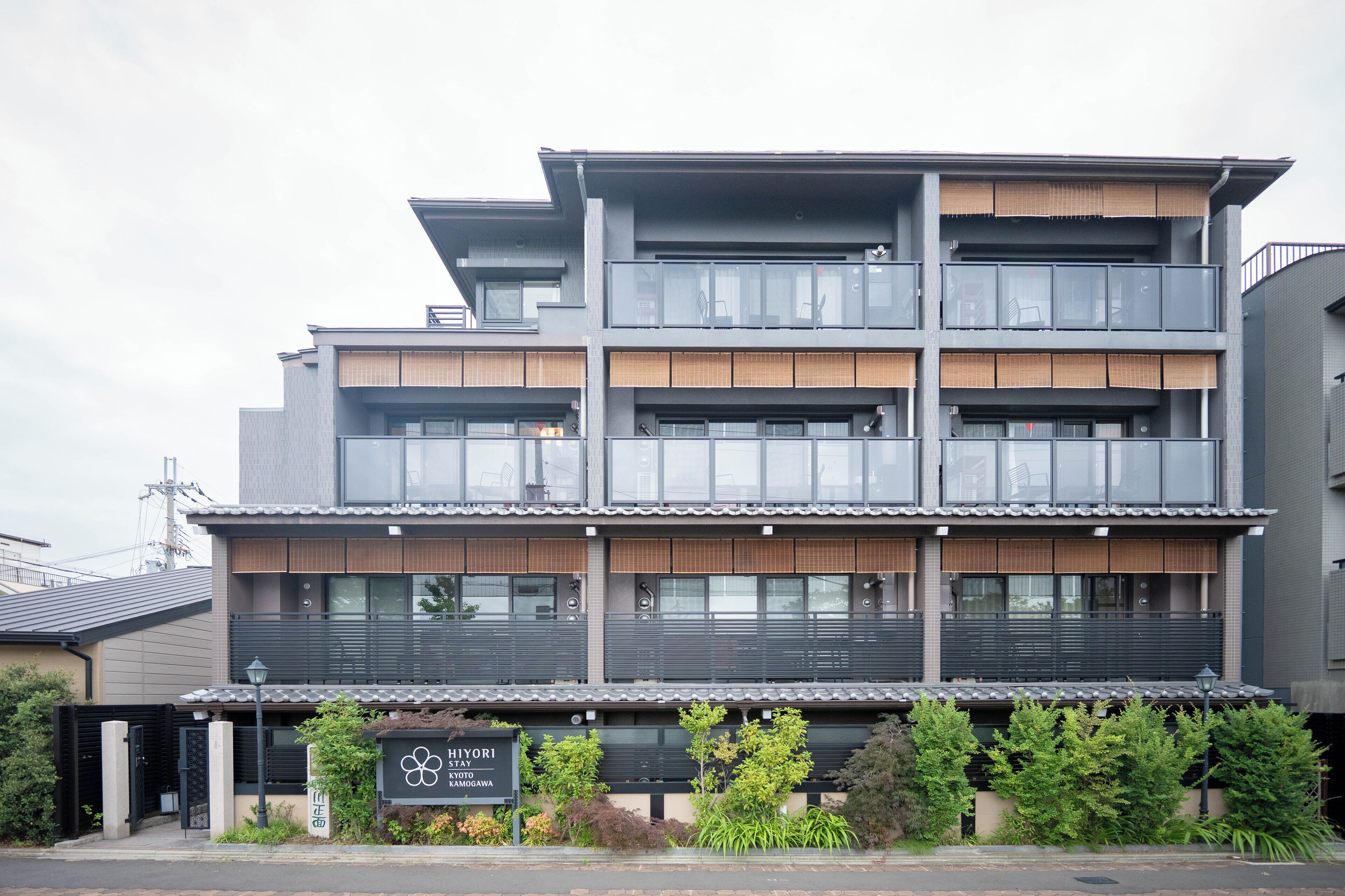 A multi-story hotel with a modern design, featuring balconies on each floor and a sign indicating it is a HIYORI STAY in Kyoto, Kamogawa.