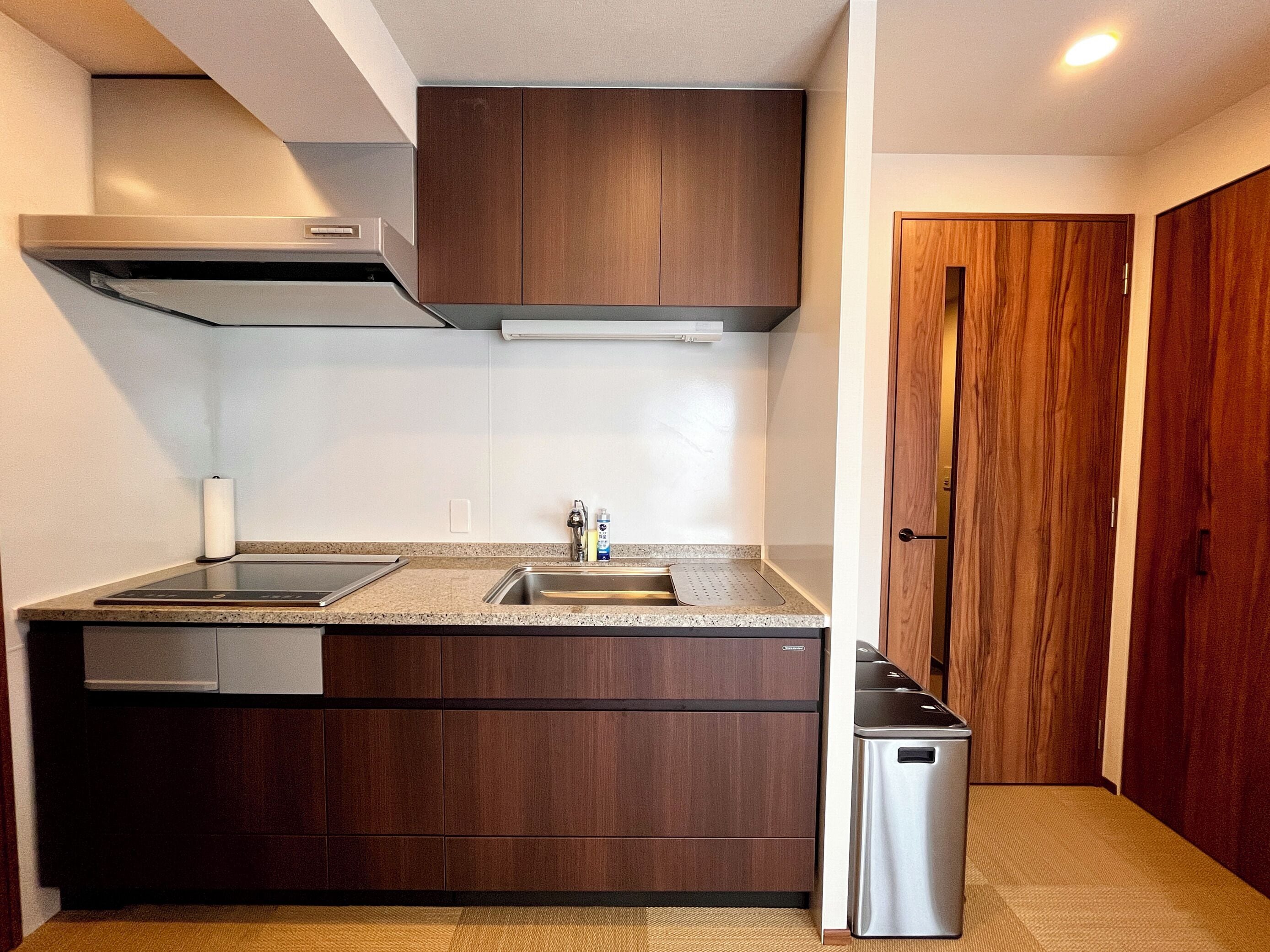 A compact kitchen with a built-in dishwasher, a stainless steel sink, and wooden cabinetry.