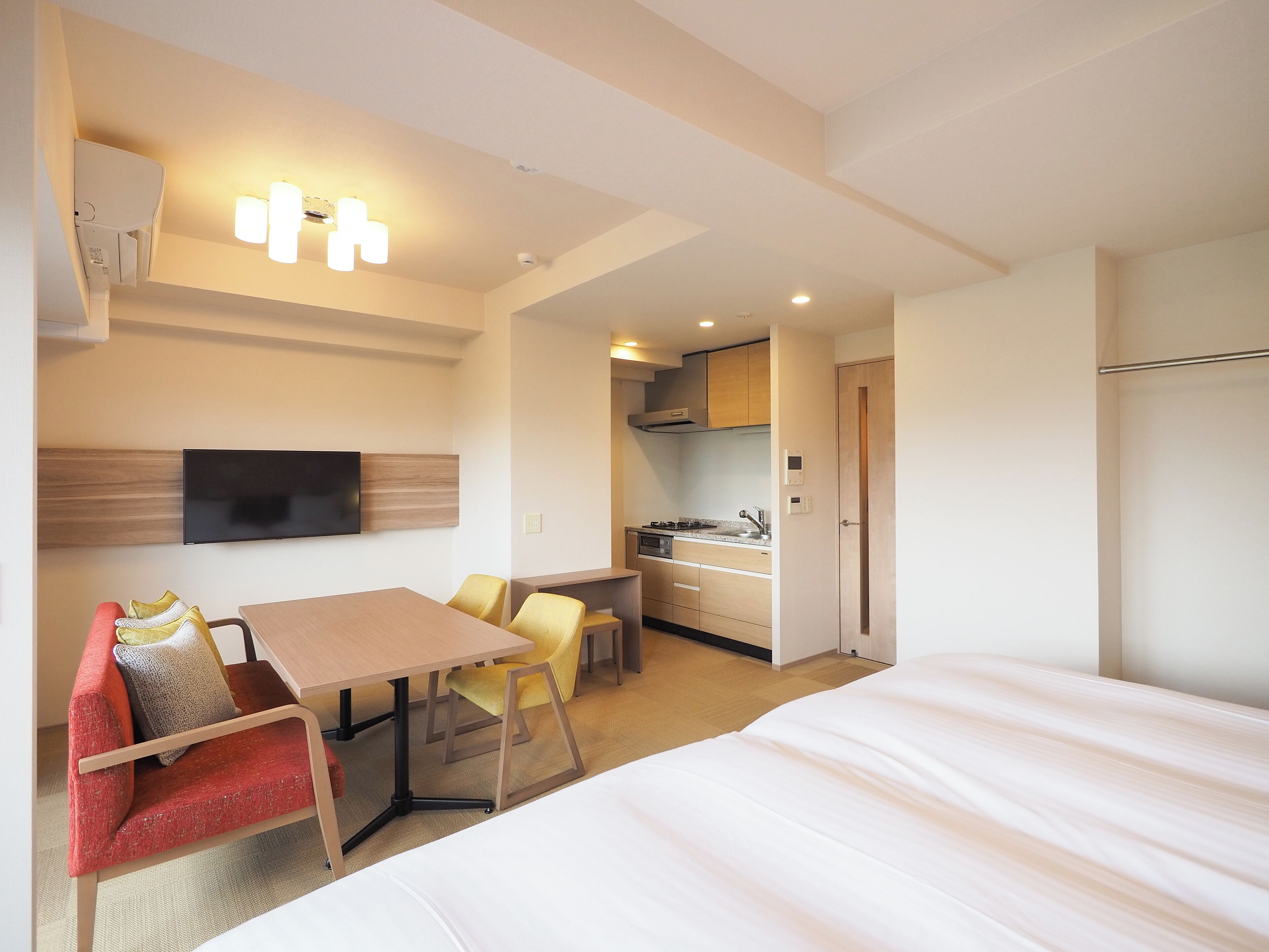 Een hotelkamer met een bed, een eettafel met stoelen, een aan de muur bevestigde televisie en een kitchenette.