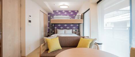 A compact hotel room with a bunk bed, a round table, and a sofa with yellow cushions.