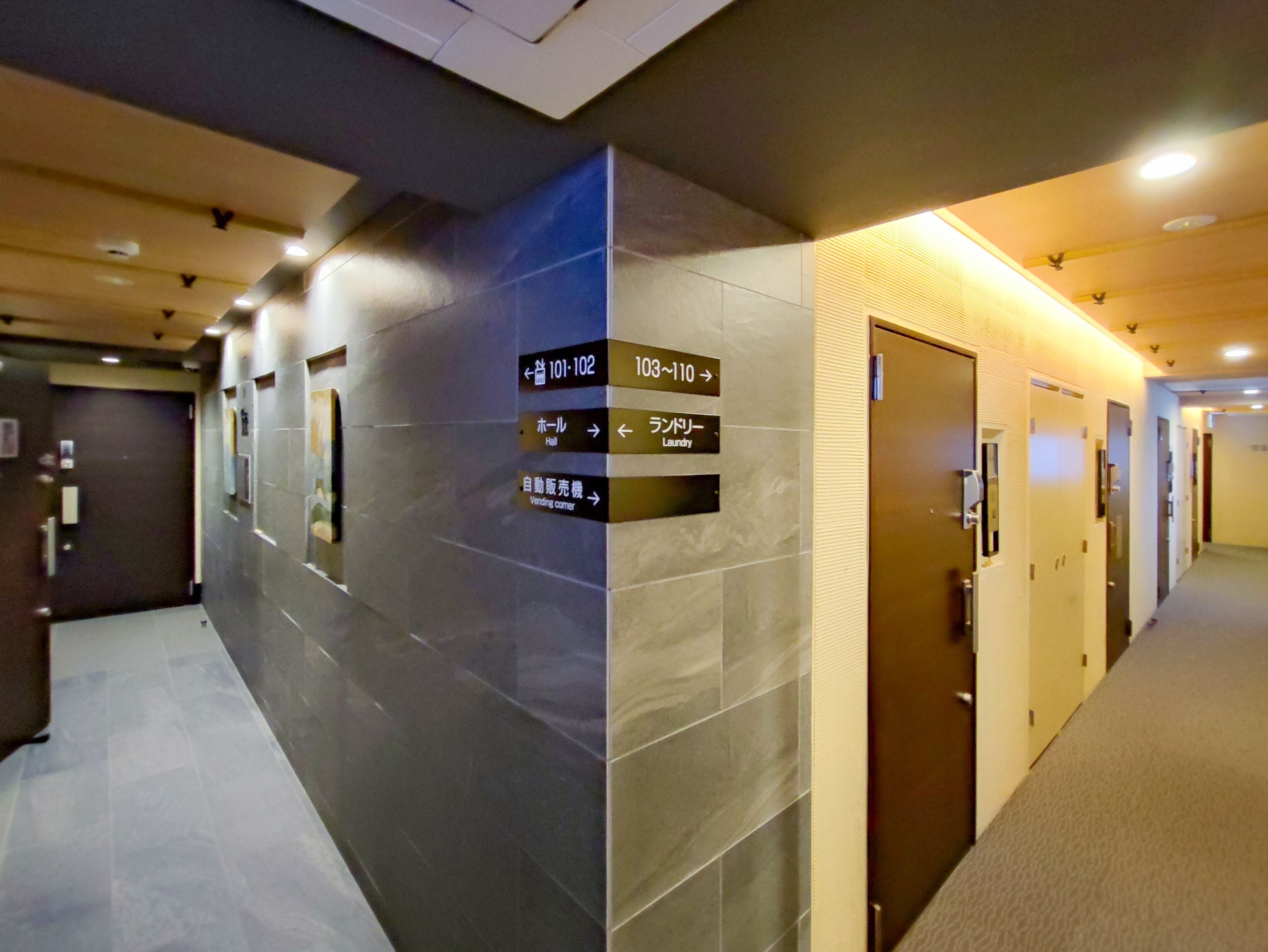 Un couloir d’hôtel avec des panneaux indiquant la direction des chambres 101-102, 103-110, d’un hall et d’un distributeur automatique.