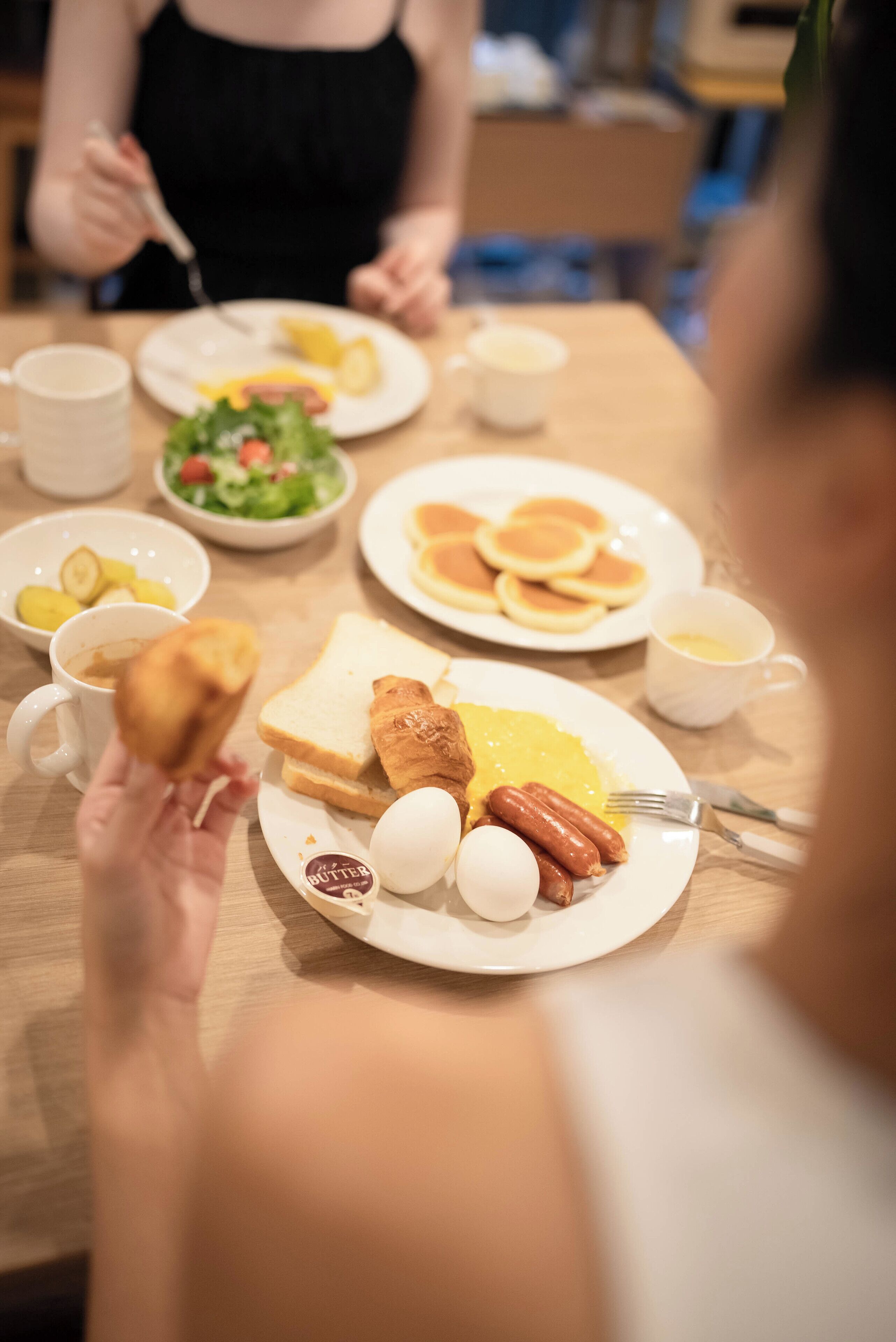 A dining table with various breakfast items including eggs, sausages, toast, and pancakes.