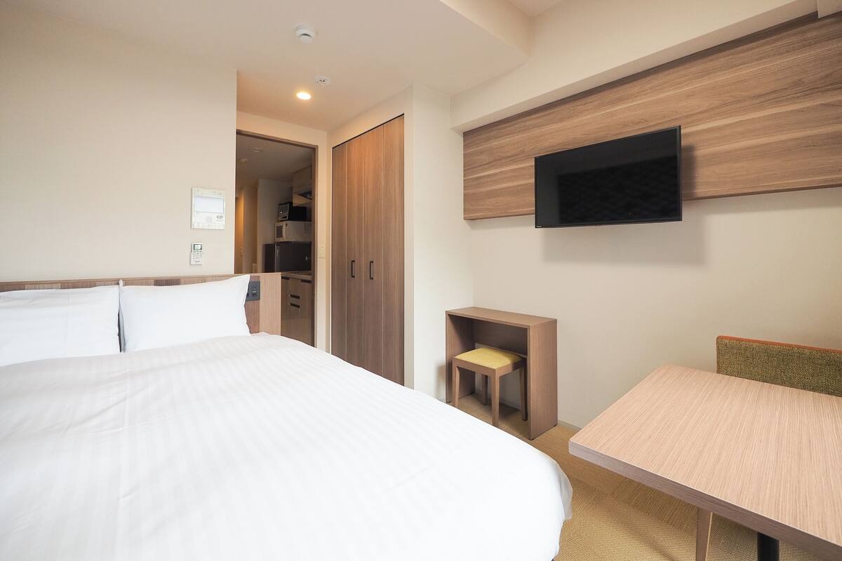 A hotel room with a large bed, a desk, a TV mounted on the wall, and a wardrobe.